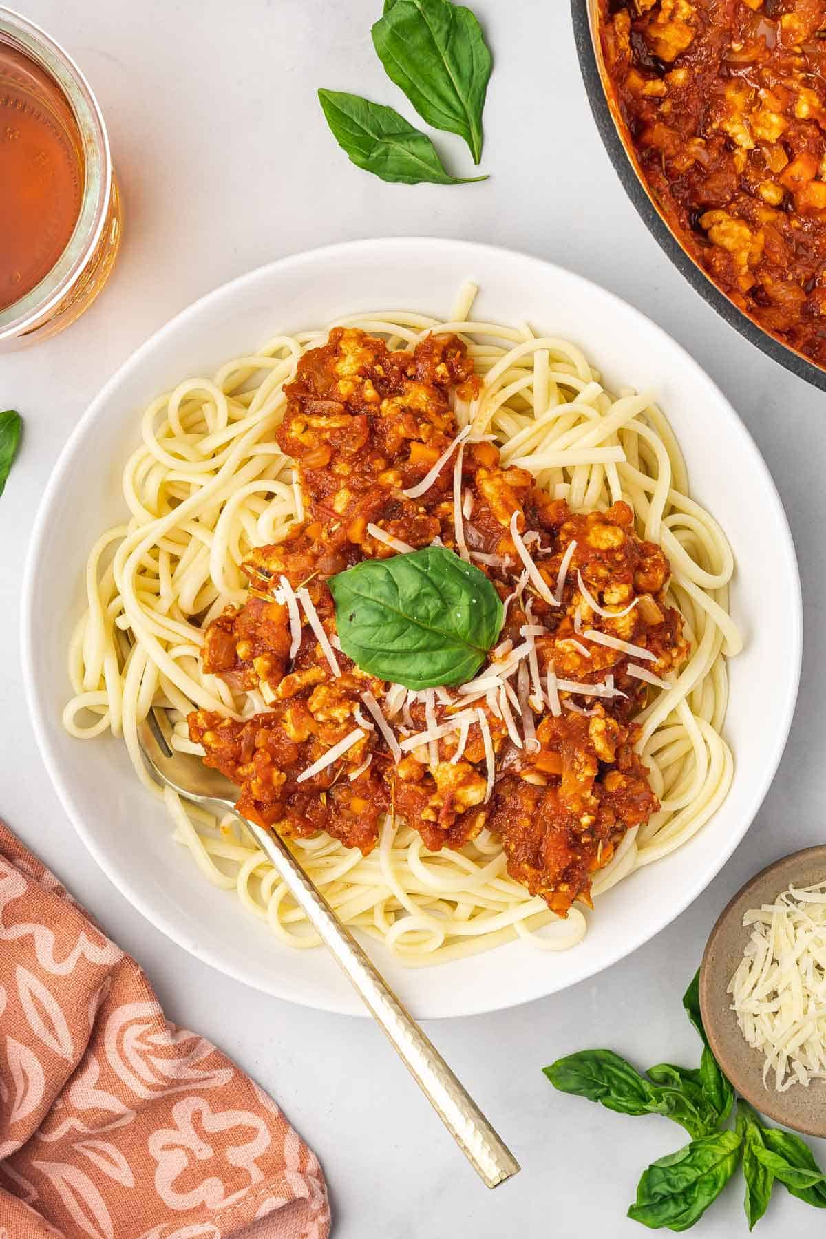 A plate spaghetti noodles with ground chicken bolognese on top with shredded cheese and fresh basil.