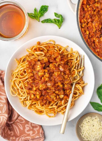 A plate of spaghetti noodles topped with ground chicken bolognese with a fork.