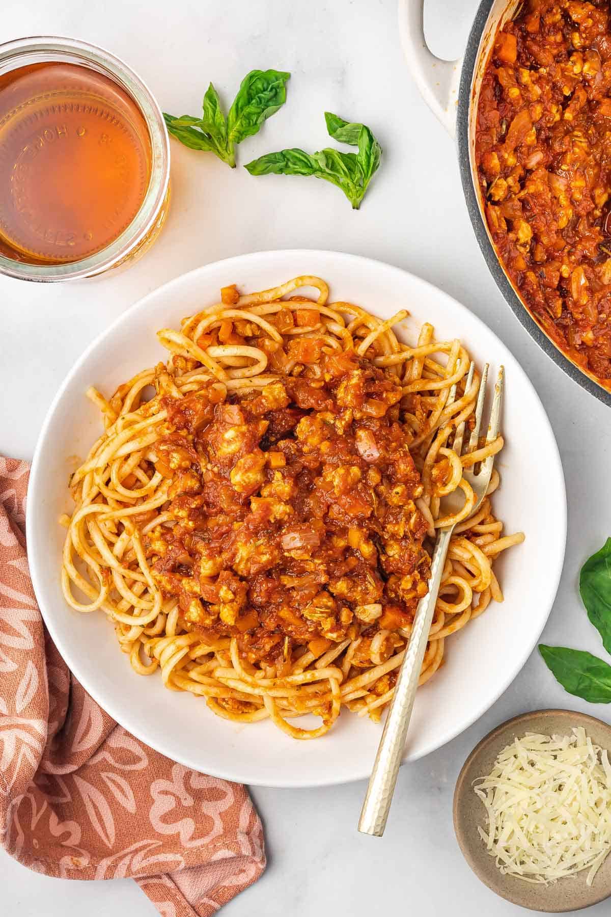 A plate of spaghetti noodles topped with ground chicken bolognese with a fork.