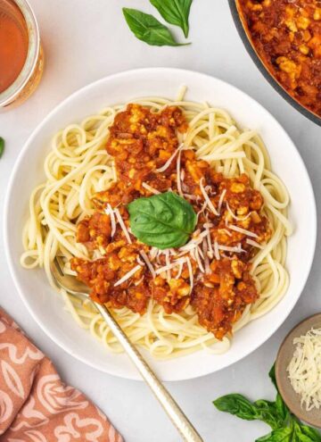 A plate spaghetti noodles with ground chicken bolognese on top with shredded cheese and fresh basil.