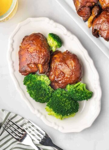 Overhead view a plate with two pieces of slow cooker bbq chicken thighs with some broccoli.