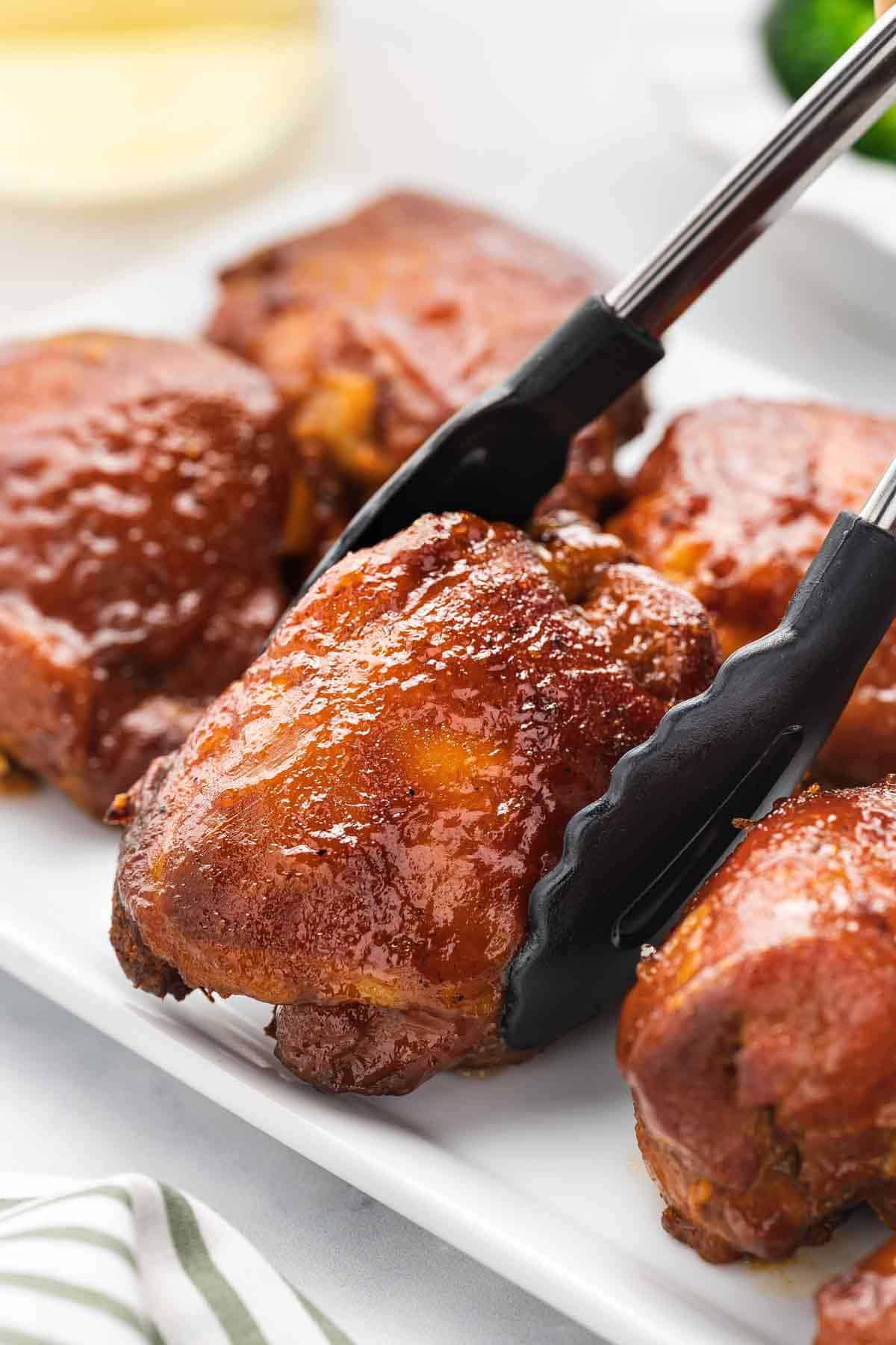 A pair of tongs placing a slow cooker bbq chicken thigh onto a platter.