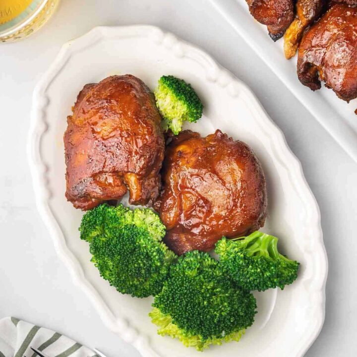 Overhead view a plate with two pieces of slow cooker bbq chicken thighs with some broccoli.
