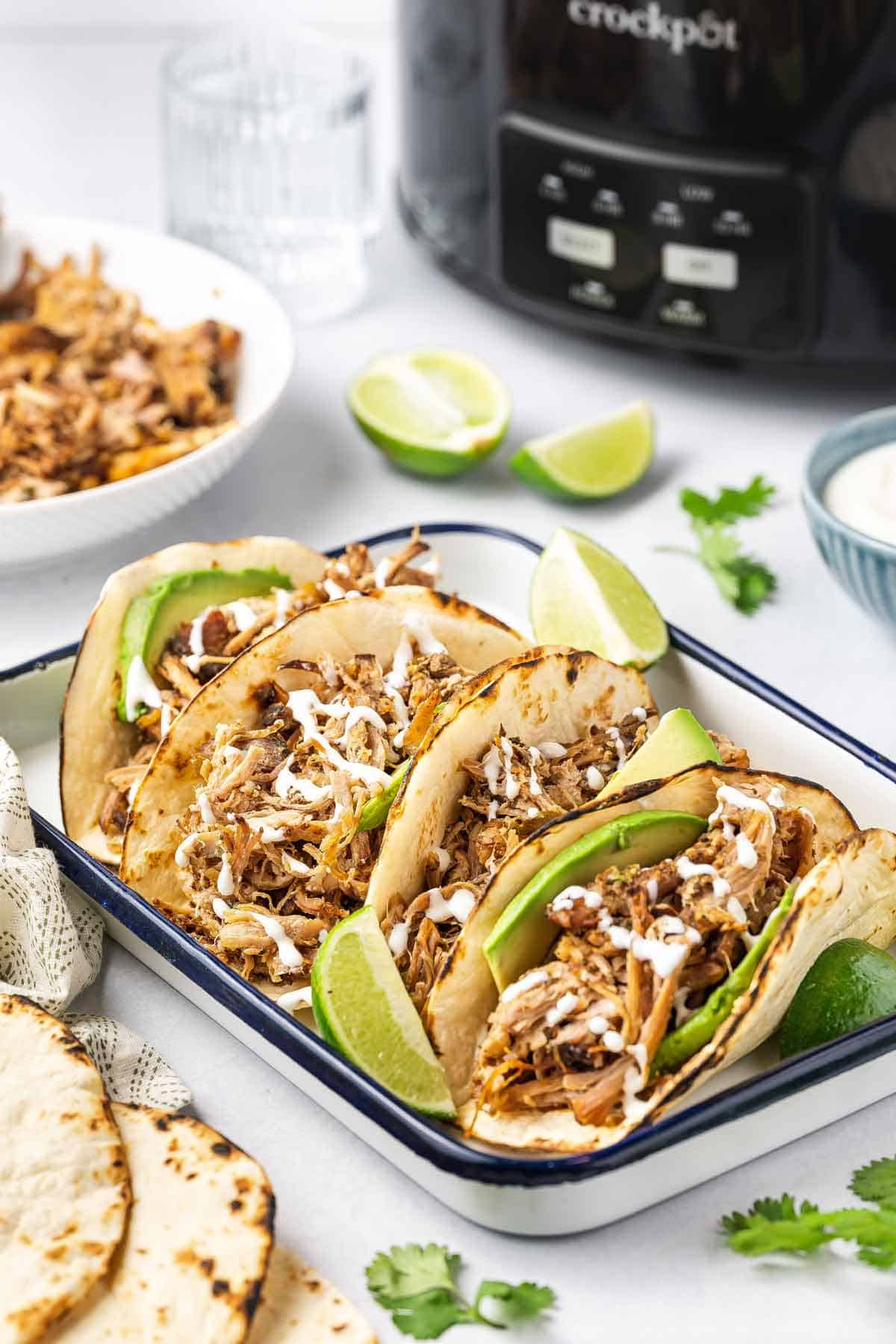 A platter of four tortillas containing shredded slow cooker carnitas.