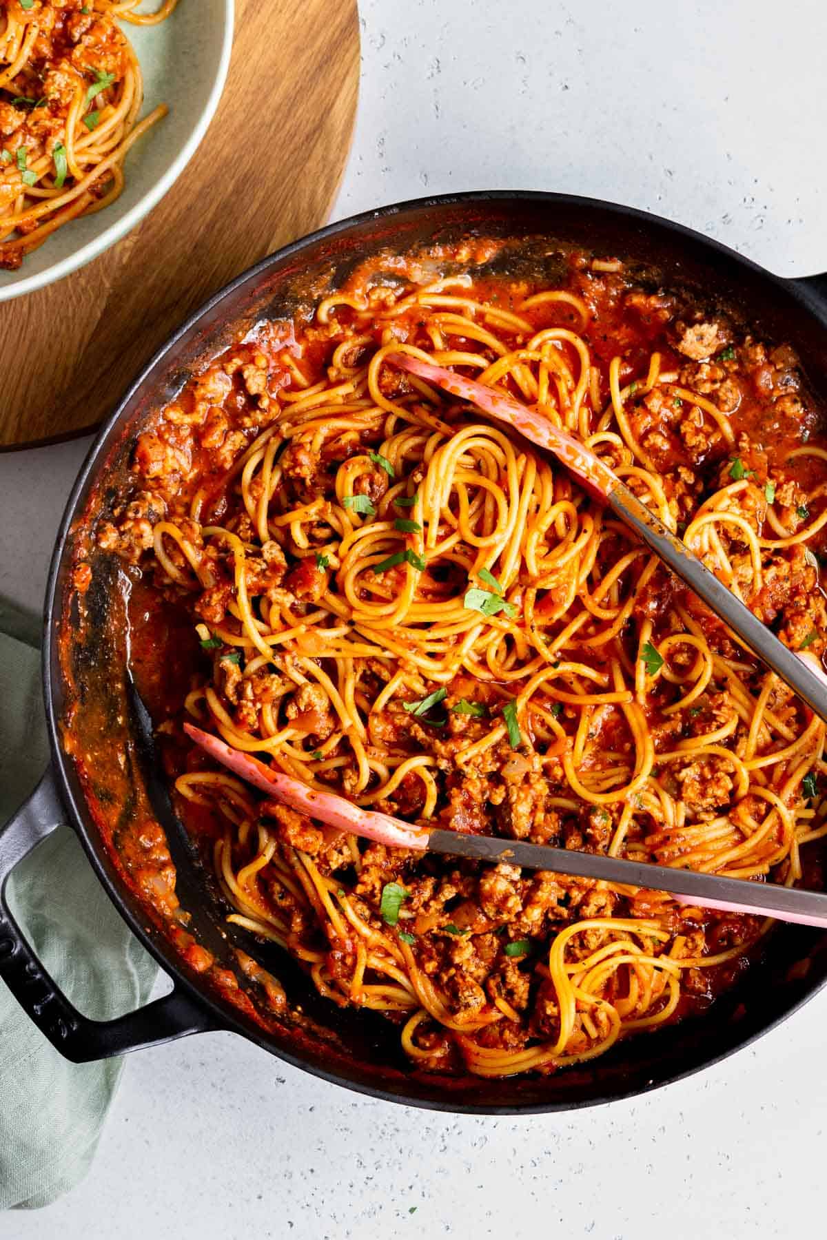 A skillet of turkey spaghetti with tongs.
