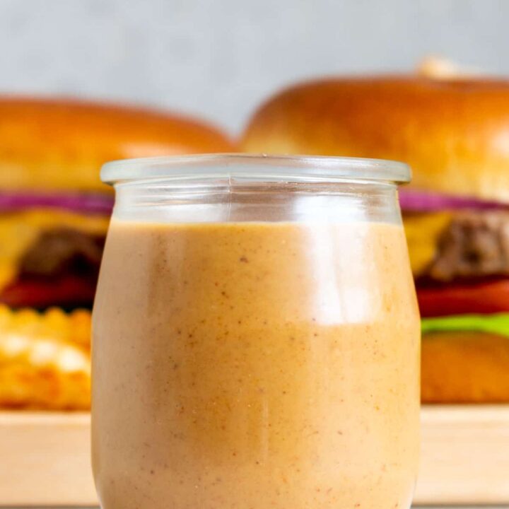 A small jar of burger sauce in front of burgers.