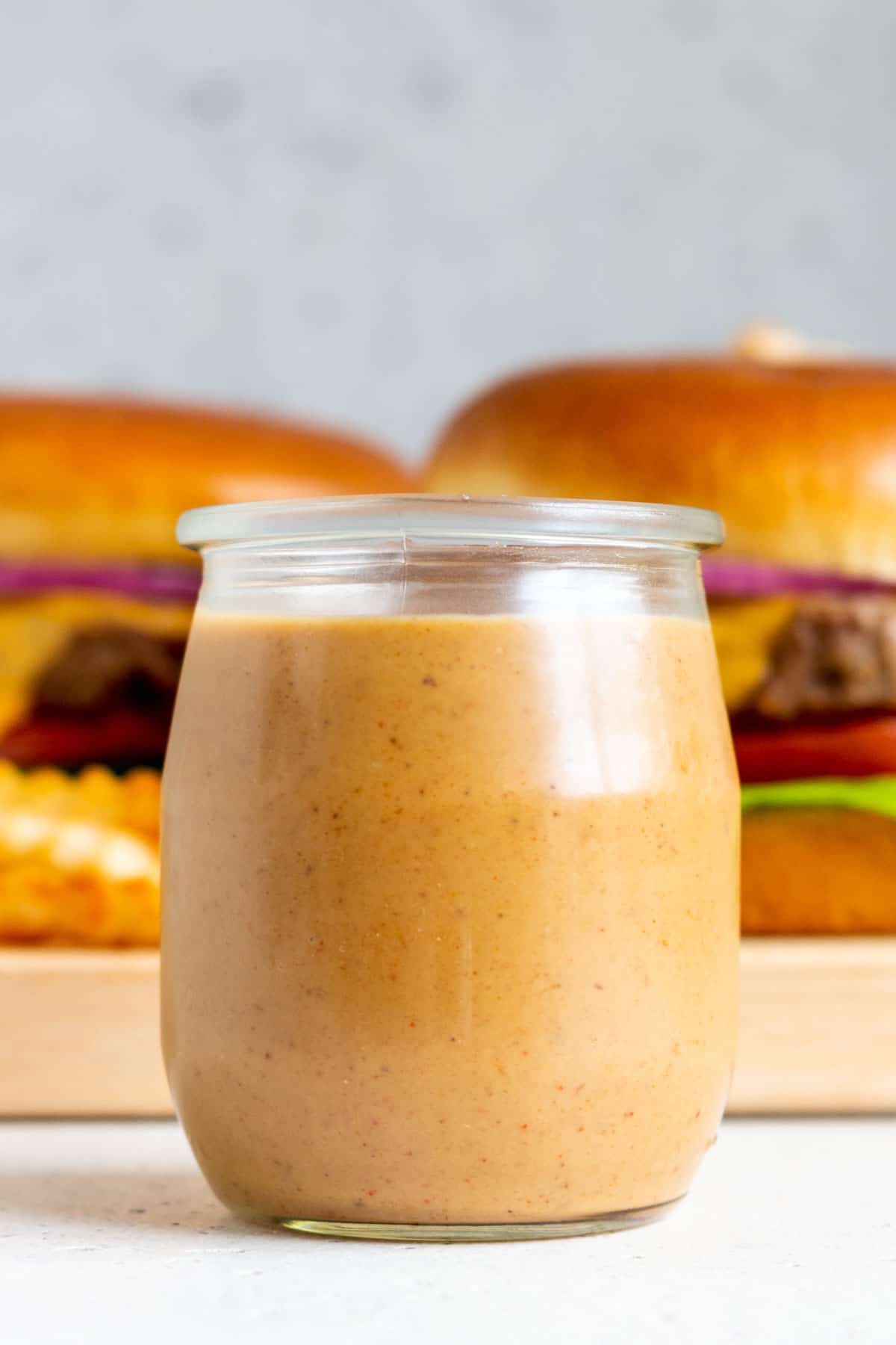 A small jar of burger sauce in front of burgers.