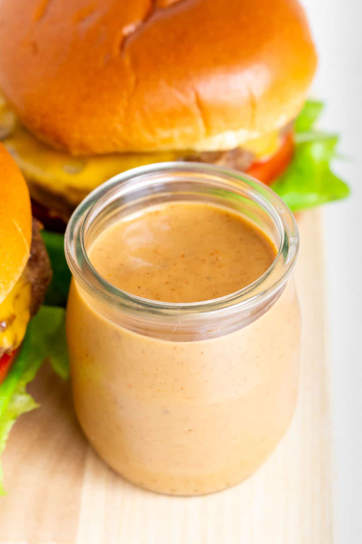 A jar of burger sauce by some burgers.