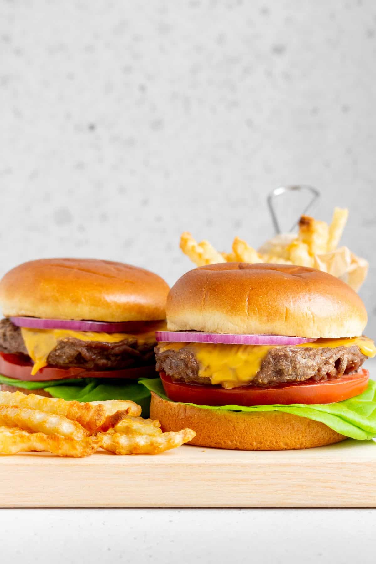 Two beef burgers on a serving board surrounded by fries.