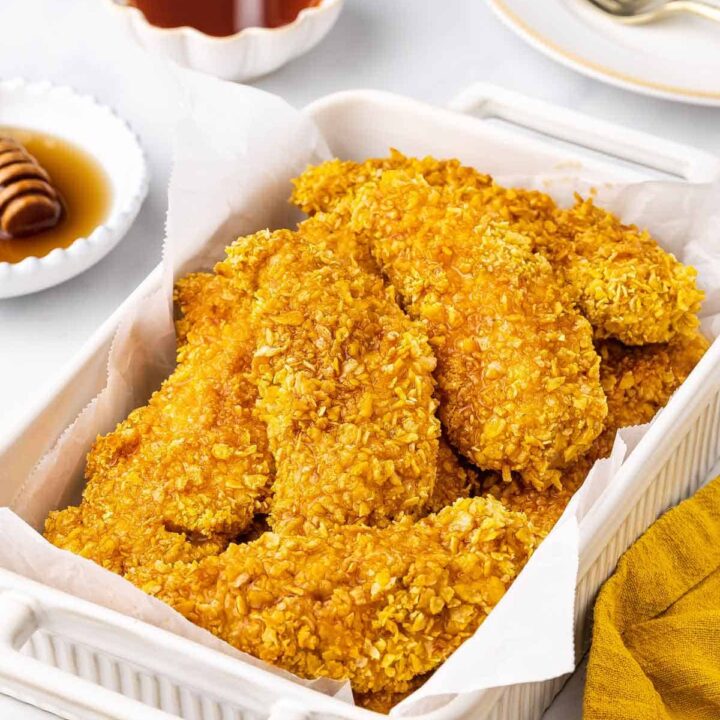 A white baking dish lined with parchment filled with hot honey chicken tenders.