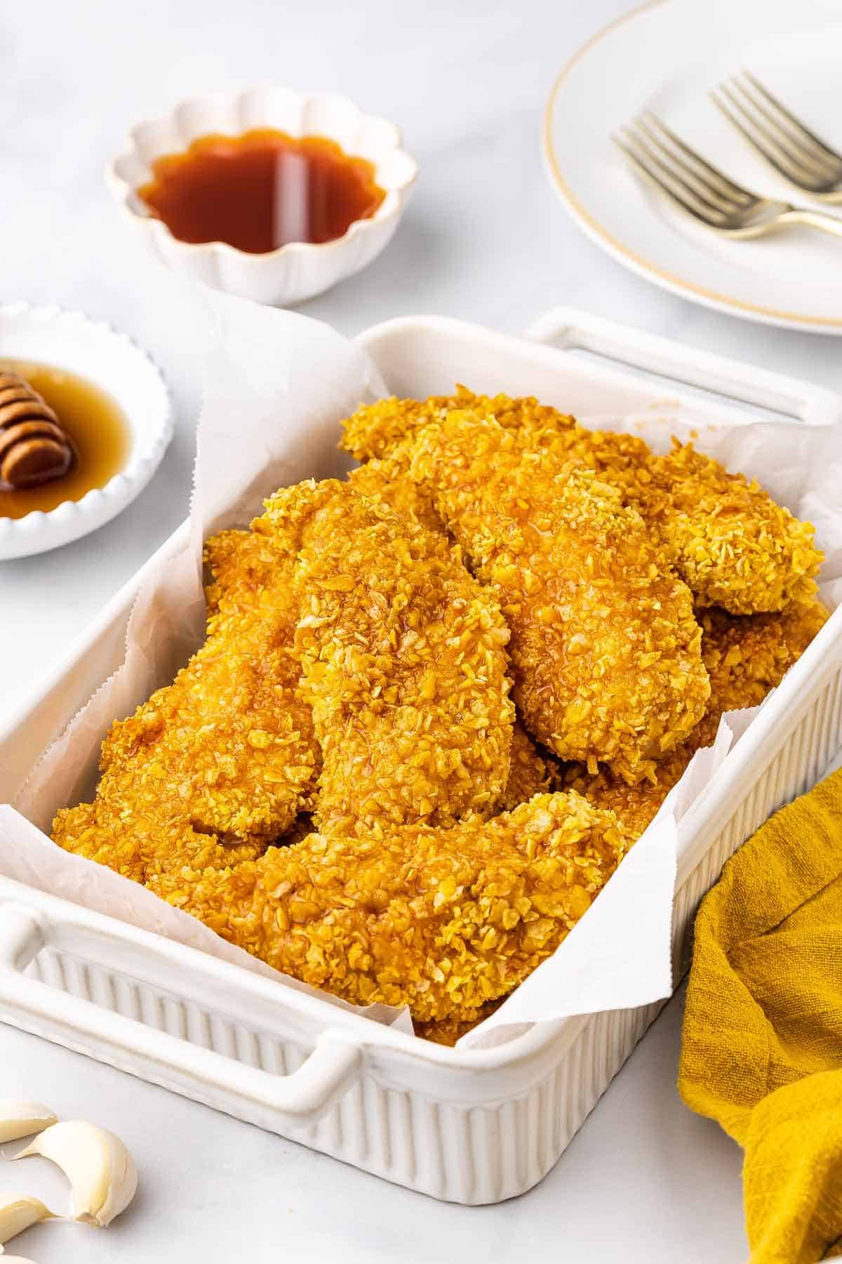 A white baking dish lined with parchment filled with hot honey chicken tenders.