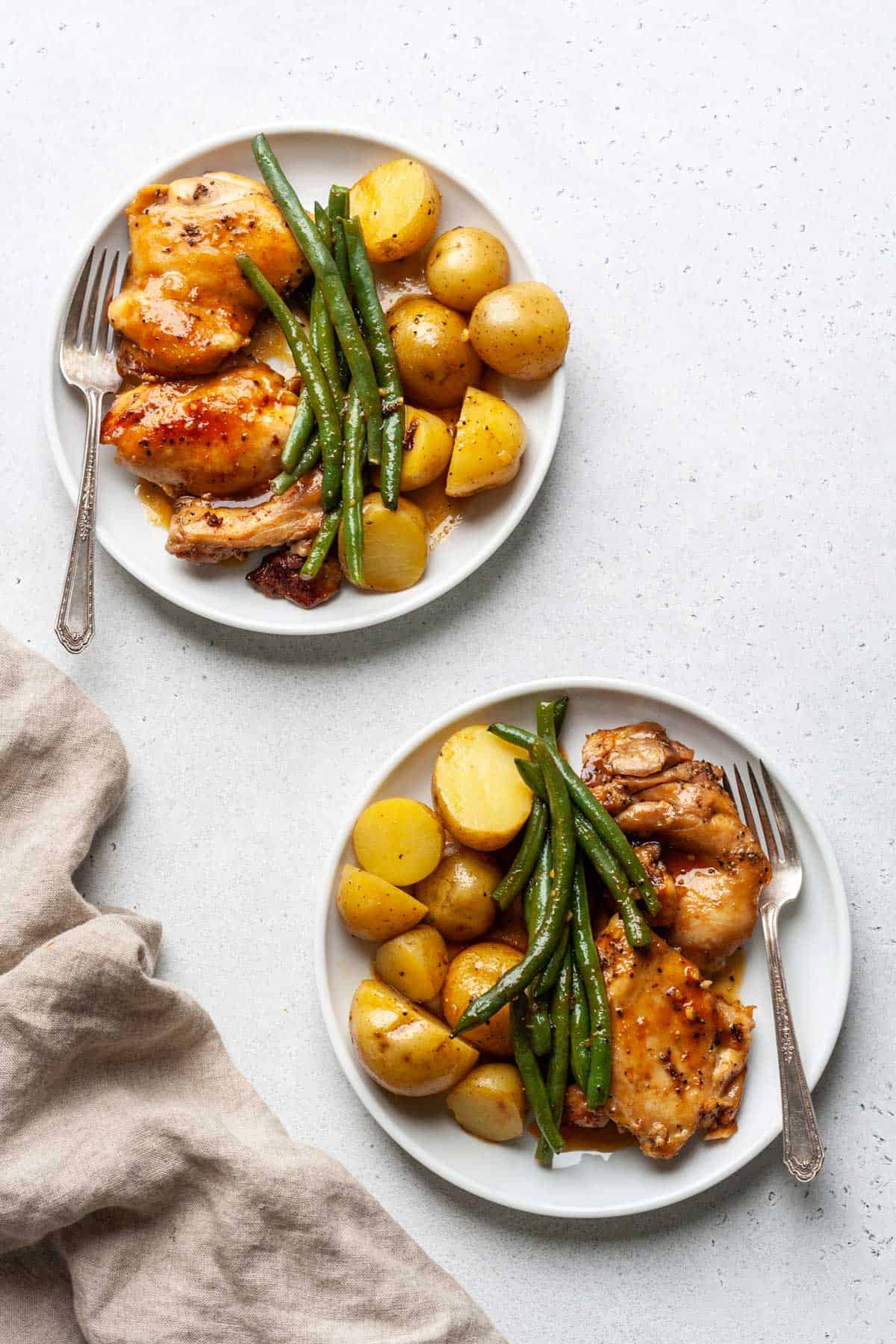 Two plates of slow cooker chicken potatoes and green beans with a fork in each plate.