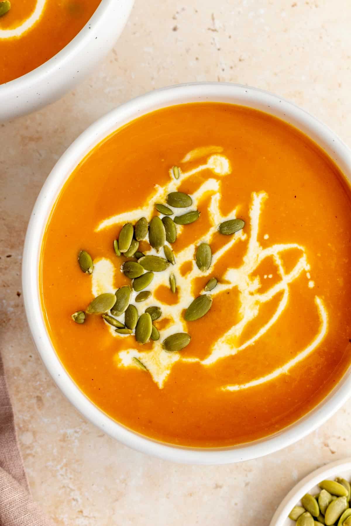 A slightly off centered view of a bowl of sweet potato and pumpkin soup garnished with coconut milk and pumpkin seeds.