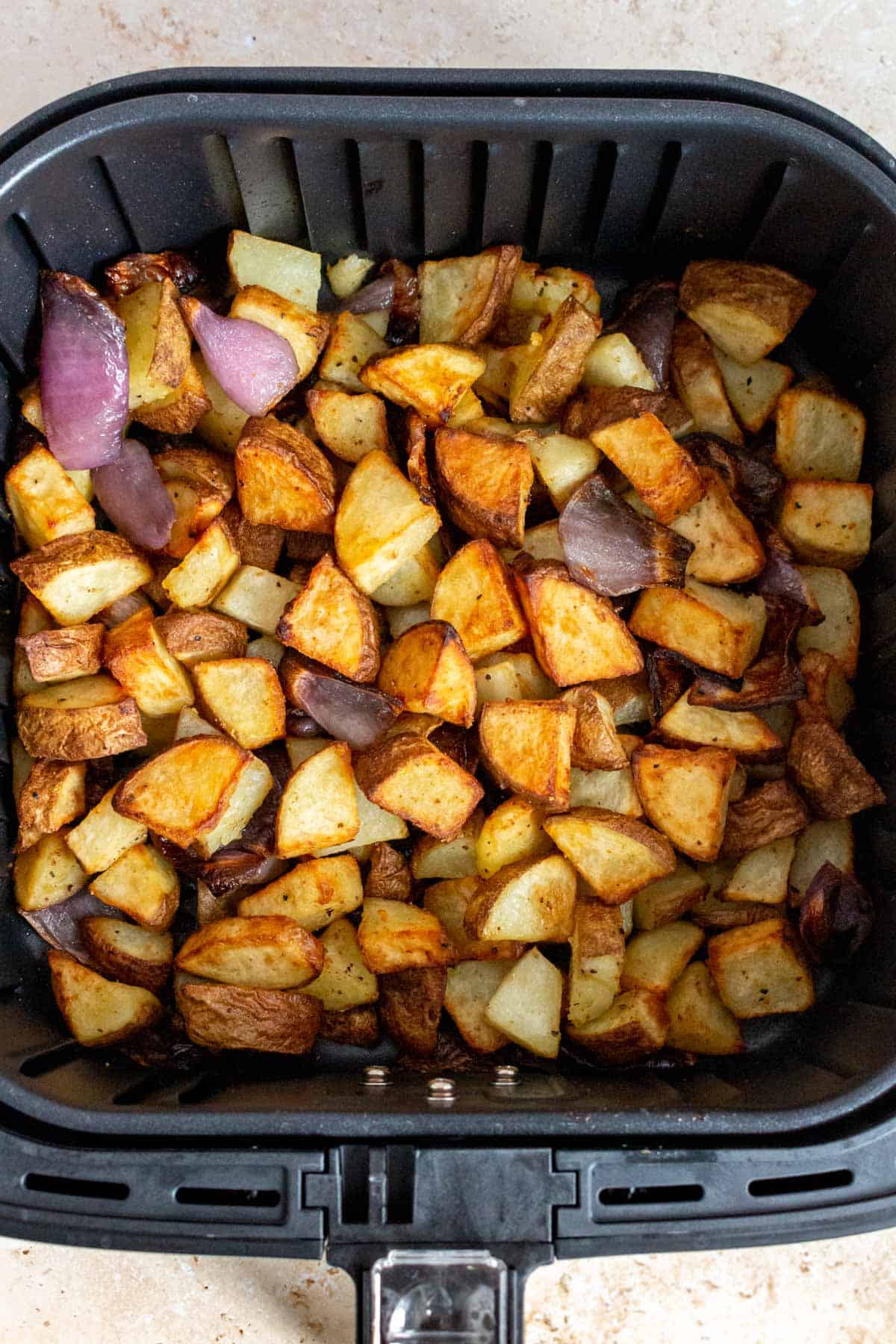 A close up view of potatoes and onions in an air fryer basket.