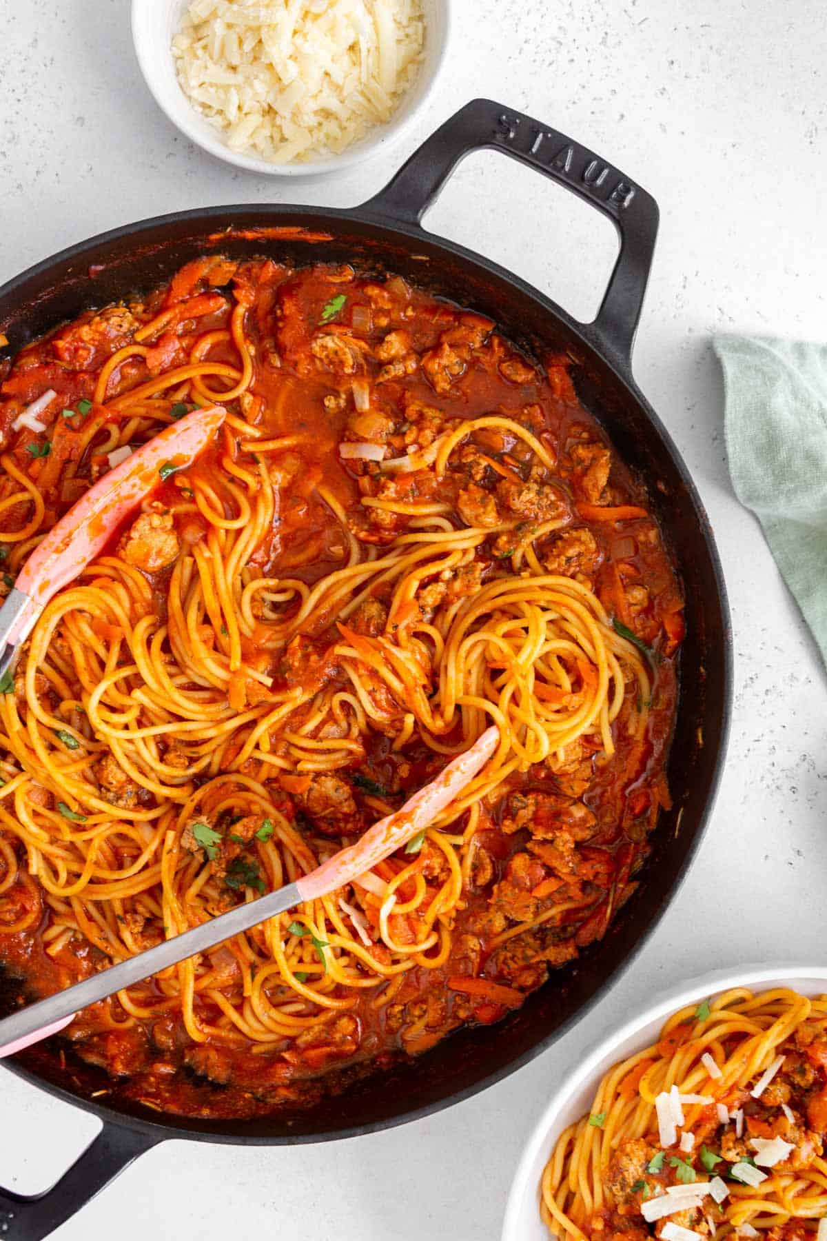 Overhead view of a skillet of one pot spaghetti with meat sauce with a pair of tongs in the skillet.