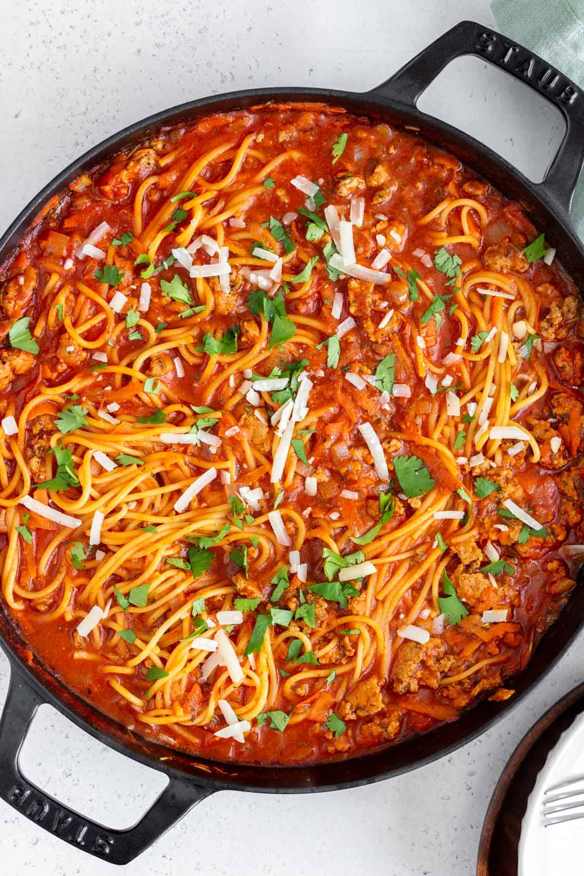 Overhead view of a skillet of spaghetti with meat sauce topped with parsley and parmesan.