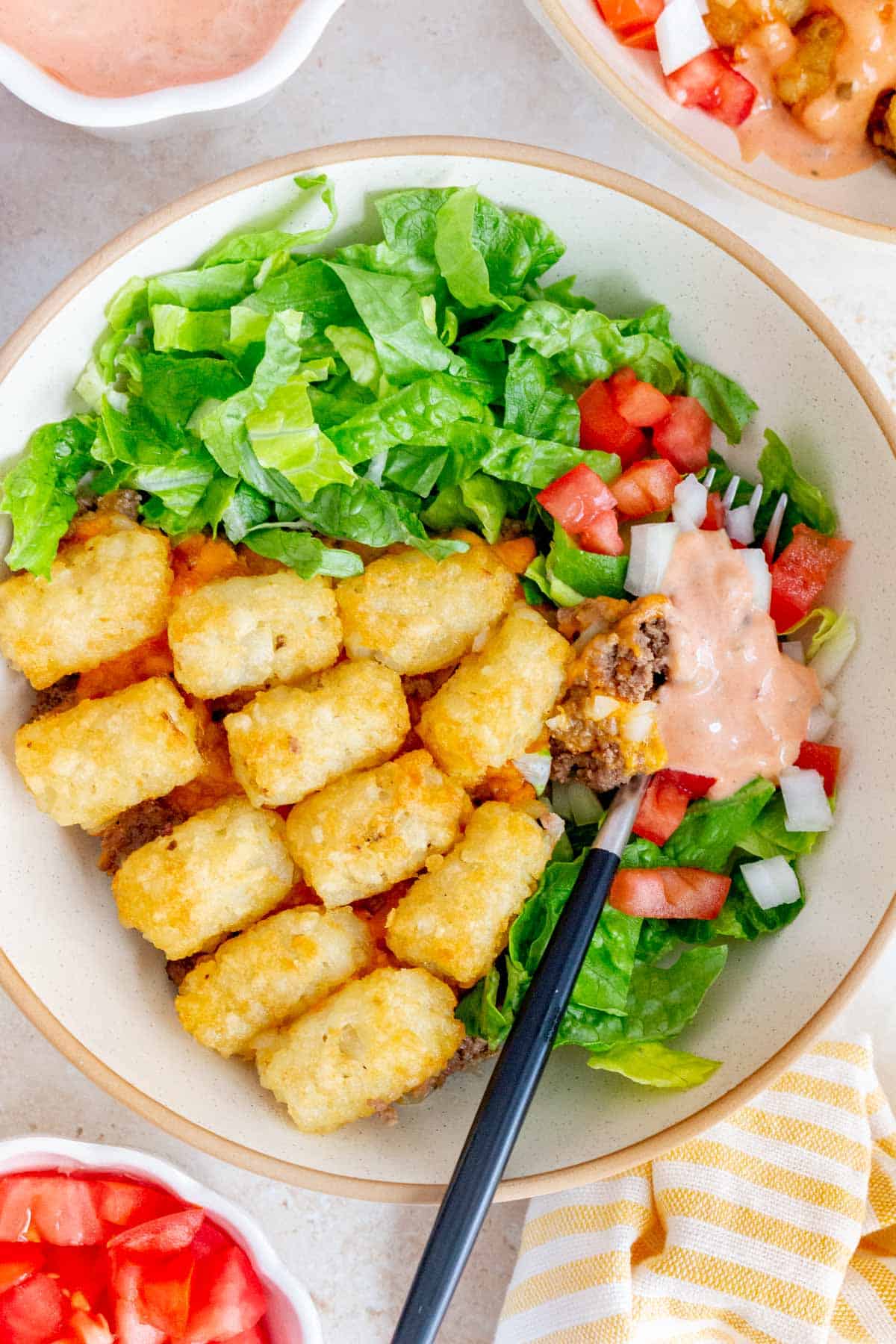 Overhead view of a bowl of big mac salad with tater tots. A fork in the bowl with sauce on top.