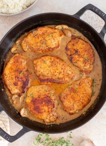 Overhead view of dutch oven pork chops smothered in sauce. Garnished with fresh thyme.