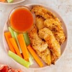 Overhead view of a plate of air fryer buffalo chicken tenders with carrots and celery along with a bowl of buffalo sauce.