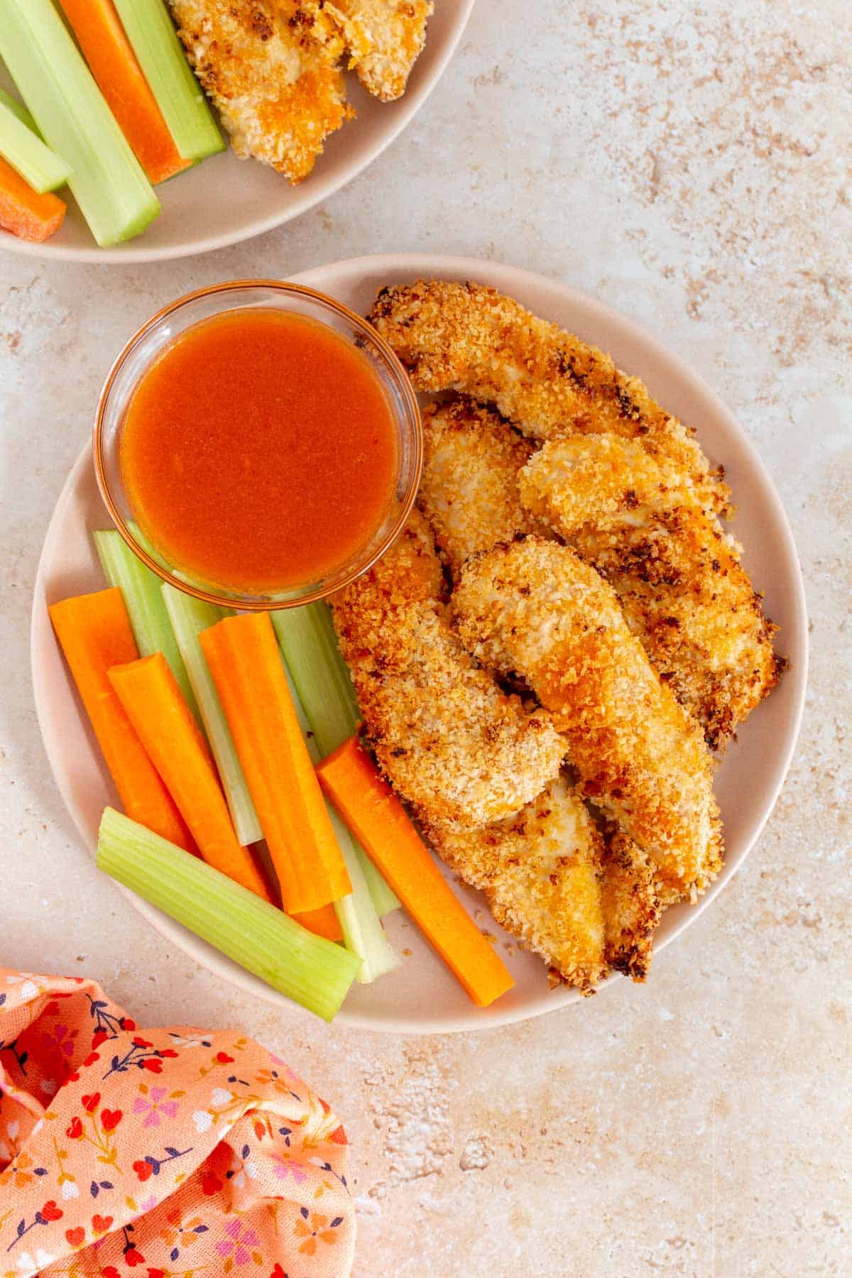 Overhead view of a plate of air fryer buffalo chicken tenders with carrots and celery along with a bowl of buffalo sauce.