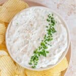 A bowl of sour cream and onion dip with chopped chives. Chips on the side.