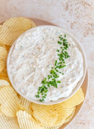 A bowl of sour cream and onion dip with chopped chives. Chips on the side.