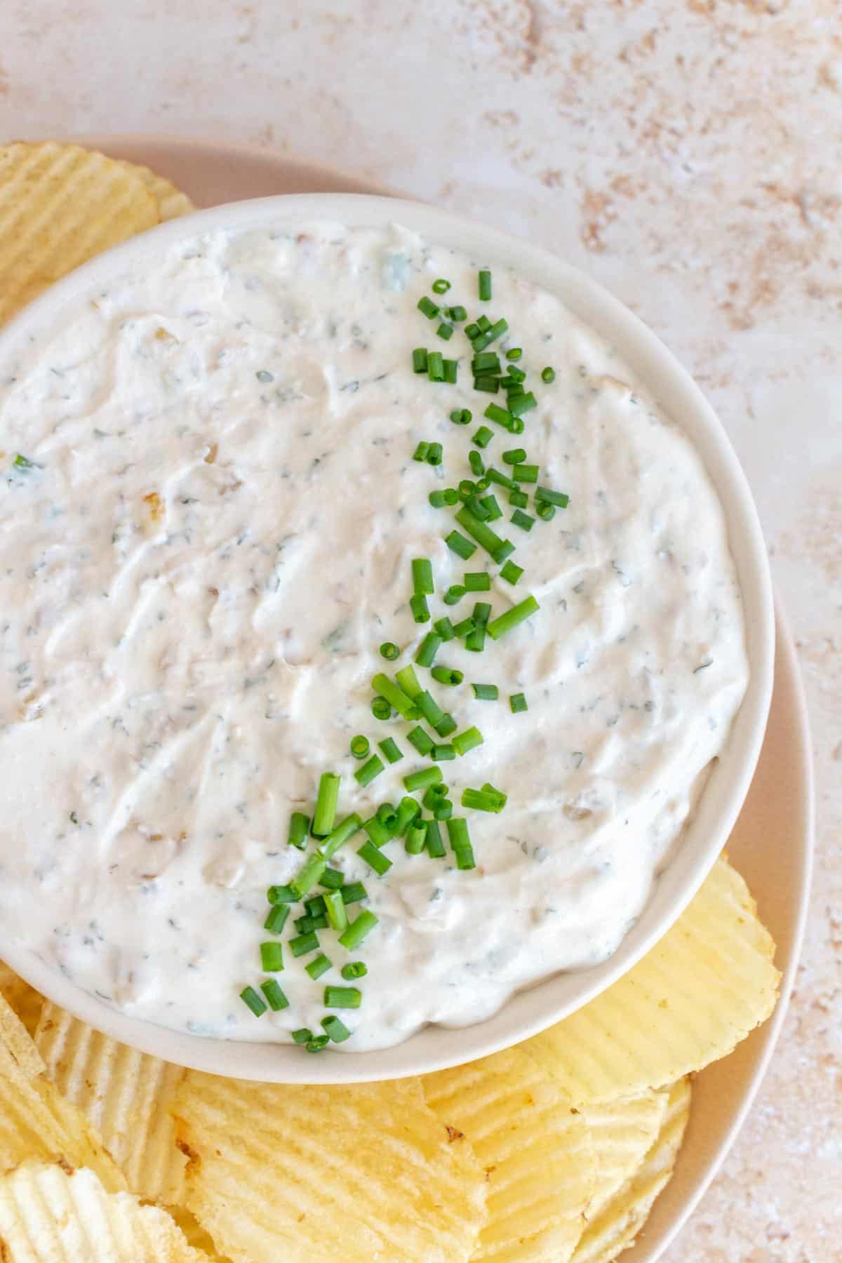 A close up view of a bowl of sour cream and onion dip topped with chopped chips.