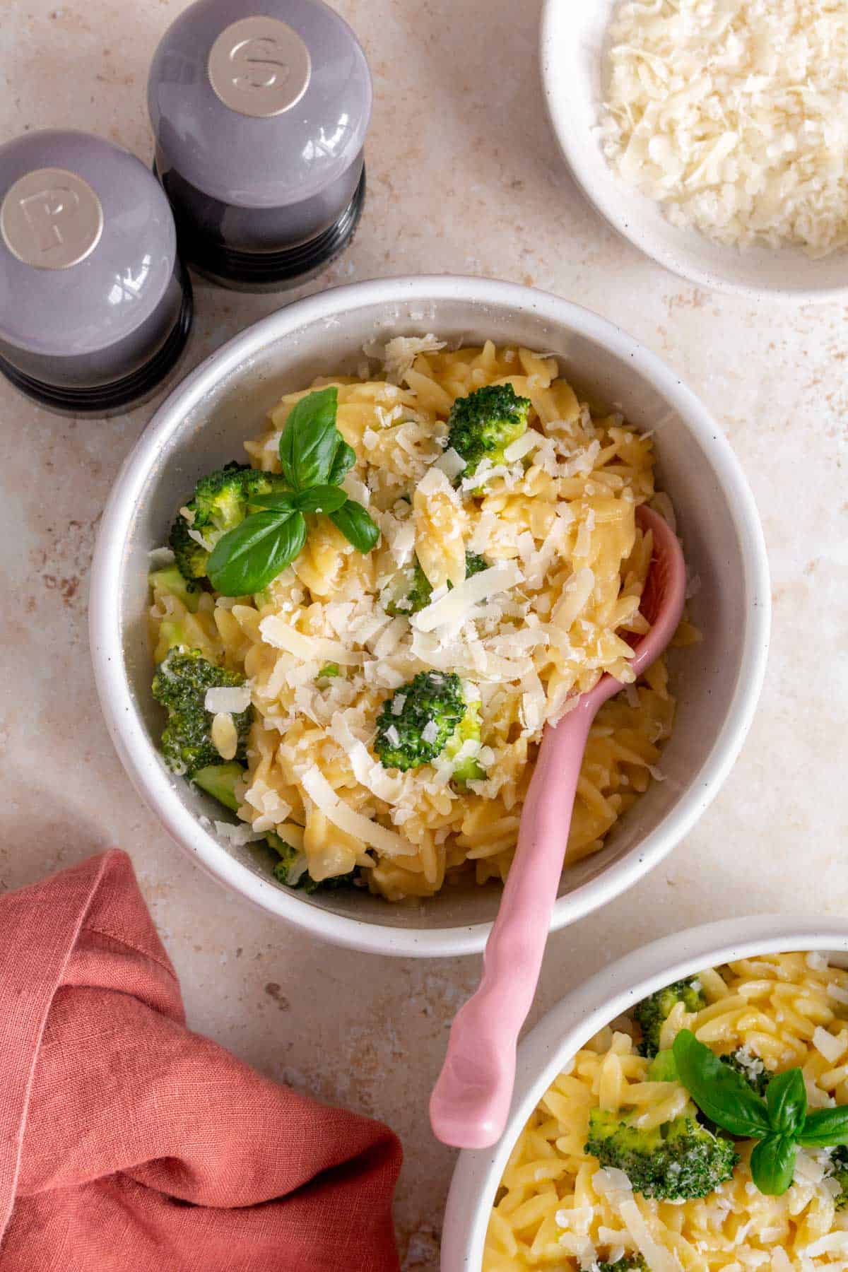 A bowl of cheesy broccoli orzo with a pink spoon inside.