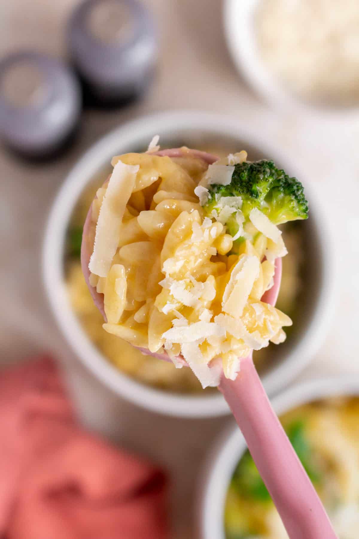 A spoonful of cheesy broccoli orzo lifted from a bowl.