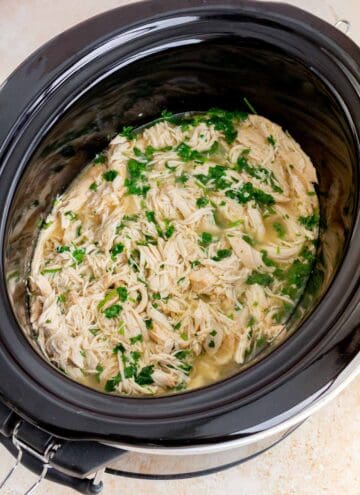 Shredded cilantro lime chicken topped with chopped cilantro in a slow cooker.