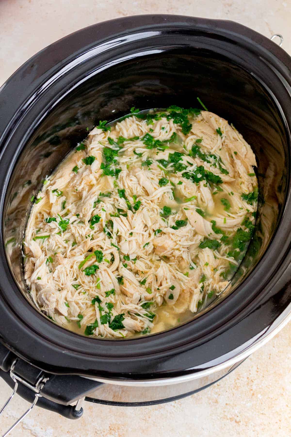 Shredded cilantro lime chicken topped with chopped cilantro in a slow cooker.