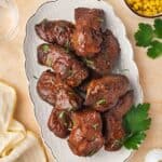 An overhead view of a platter of slow cooker country style ribs with some parsley garnish. A small bowl of corn on the side.