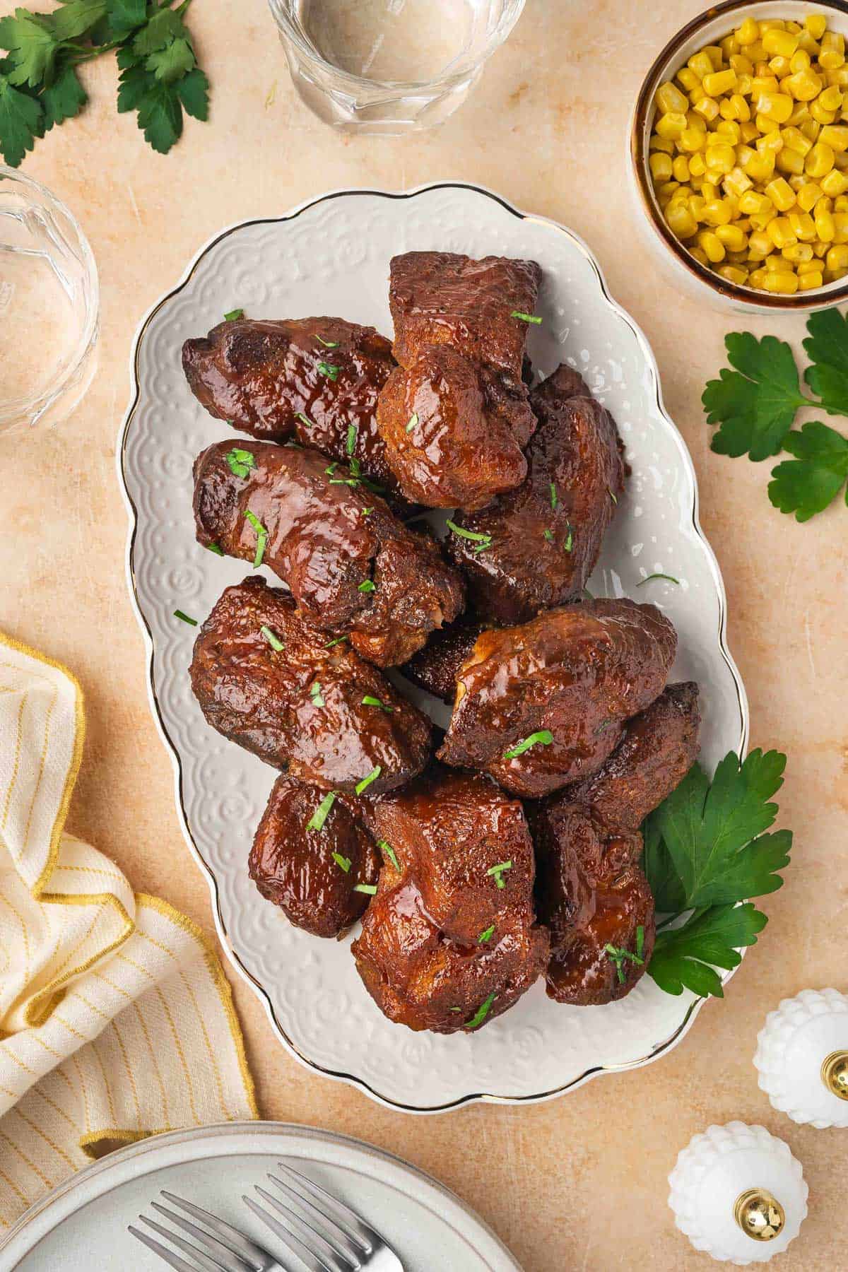 An overhead view of a platter of slow cooker country style ribs with some parsley garnish. A small bowl of corn on the side.