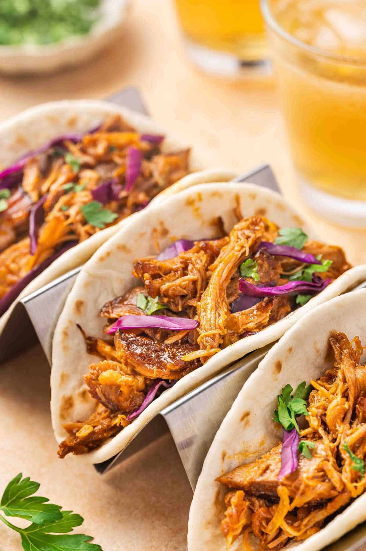 A taco holder with three tacos with crockpot gochujang pulled pork inside of the tortillas.
