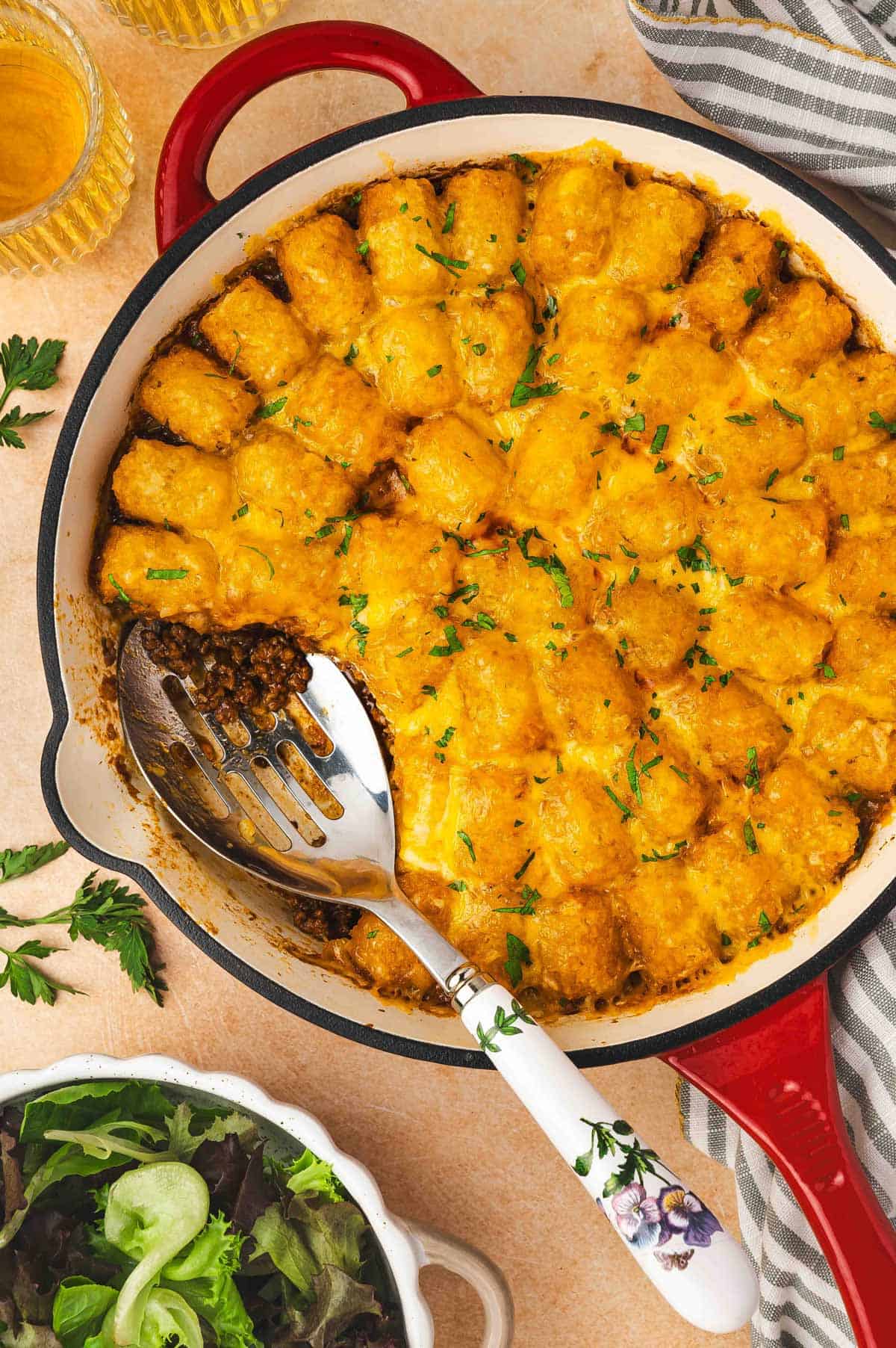 Overhead view of sloppy joe tater tot casserole in a cast iron skillet with a portion scooped out.