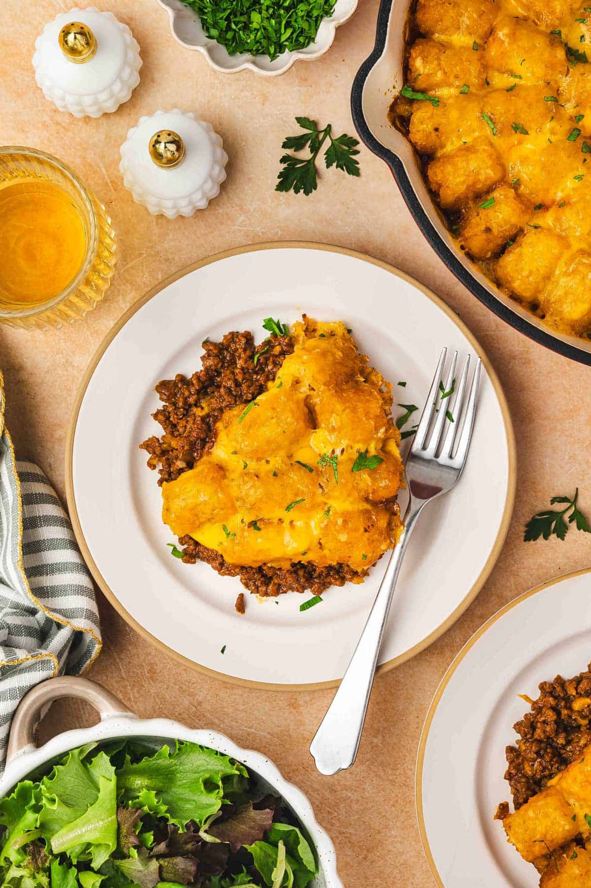 Overhead view of a plate with a serving of sloppy joe tater tot casserole topped with parsley garnish and a fork.