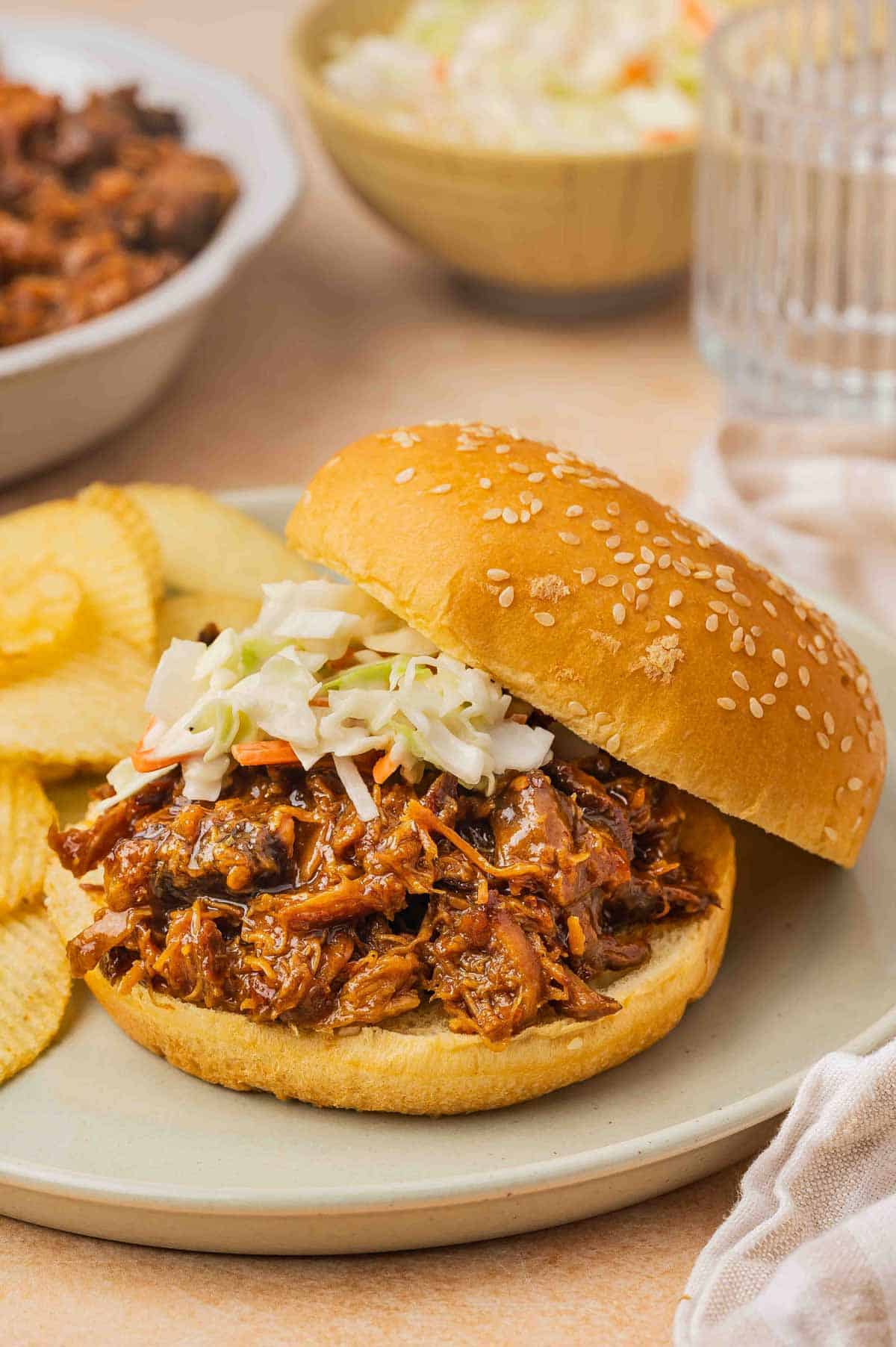 A plate with slow cooker hot honey chicken on a burger bun with coleslaw on top.
