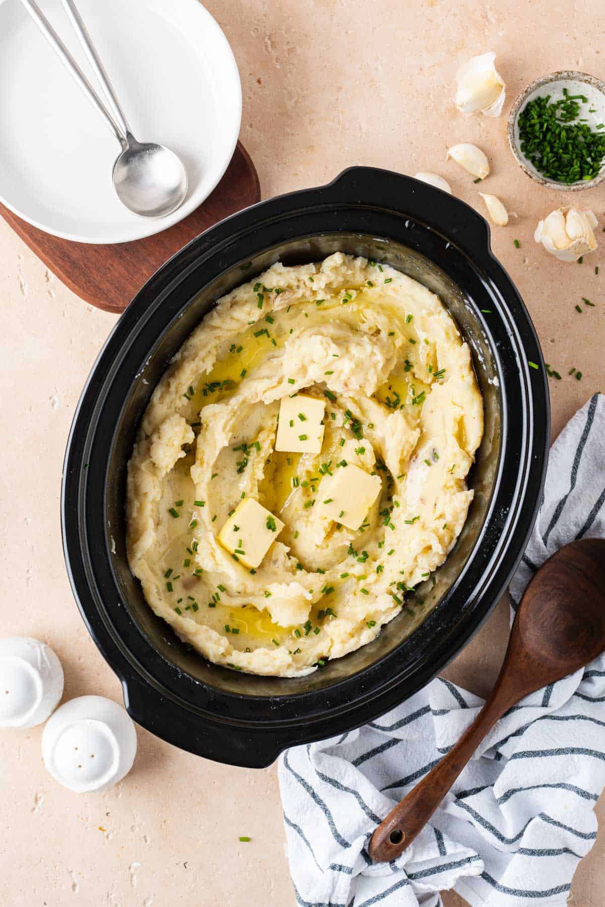 Overhead view of a crockpot with mashed potatoes topped with butter and chives.